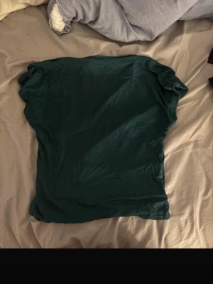 Mörkgrön topp med öppen rygg - En enkel mörkgrön topp i mjukt material med korta ärmar och snygg öppen rygg. Perfekt till jeans eller kjol för en avslappnad look. Tunn och skön att bära, passar bra till varmare dagar.