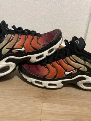 Nike Air Max Plus TN färgskiftande - Nike Air Max Plus TN sneakers med färgskiftande mesh i rött, orange, gult och grönt. Svarta detaljer och vita sidoswooshes. Tjock vit sula med synliga luftbubblor och svarta vågformade linjer på ovandelen. Klassisk streetwear-look och riktigt snygg design.