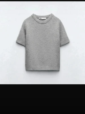 Grå stickad t-shirt från Zara - Säljer en stilren grå stickad t-shirt från Zara med rund halsringning och korta ärmar. Tröjan har en enkel och clean design, perfekt för dig som gillar minimalistiskt mode. Materialet känns mjukt och bekvämt mot huden.