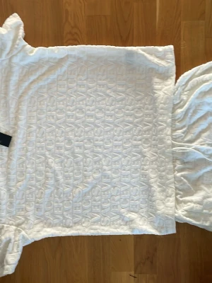 Vit Versace outfit set   - Säljer en vit t-shirt från Versace med upphöjt reliefmönster där Versace-loggan upprepas över hela plagget. Klassisk rund halsringning och korta ärmar. Materialet känns mjukt och exklusivt, perfekt för dig som gillar lyxiga detaljer.