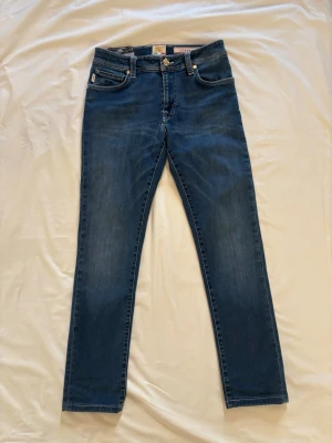 Blå jeans från Tramarossa - Snygga blå jeans från Tramarossa med klassisk femficksmodell och raka ben. Jeansen har diskreta slitningar och detaljerade sömmar. Tillverkade i mjukt jeansmaterial med knappgylf och patch med logga i midjan.