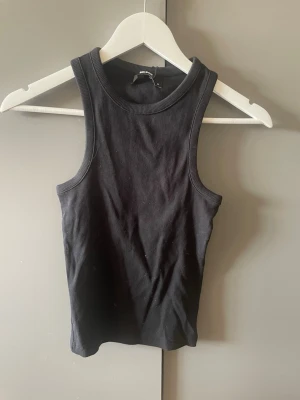Svart ribbad linnetopp från Bik Bok - Snygg svart ribbad linnetopp från Bik Bok i storlek M. Toppen är ärmlös med rund halsringning och croppad passform. Perfekt att styla med jeans eller kjol för en trendig look.