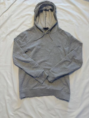 Grå hoodie från A.P.C. - Snygg grå hoodie från A.P.C. med klassisk huva och dragsnören. Tillverkad i mjukt material och har diskret logga på bröstet. Perfekt för en avslappnad och stilren look. Tillverkad i Portugal.