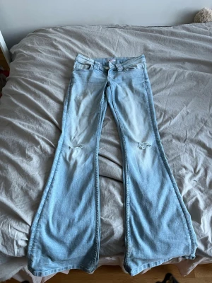 Ljusblå bootcut jeans - Säljer ett par ljusblå bootcut jeans med slitningar vid knäna. Anledningen för att jag säljer de är för att de inte kommer till användning, har använt kanske tio gånger max