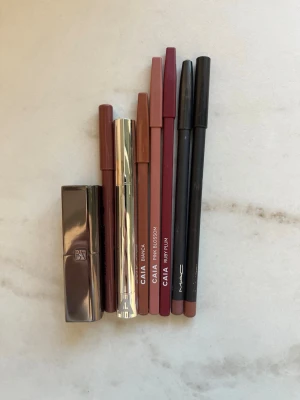 Läppennor i nude och bruna toner - Säljer ett set med läppennor från CAIA och MAC i olika nude, bruna och rosatoner. Pennorna har klassisk form och är perfekta för att definiera läpparna. Färgerna inkluderar Spice från MAC samt Bianca, Pink Blossom och Ruby Plum från CAIA. Materialet är trä med plastlock. Vissa är mer använda än andra men fortfarande i fräckt skick! Allt på bilden ingår och säljs som ett set 