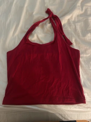 Röd halterneck topp med knyt - Snygg röd halterneck topp med knyt i nacken. Toppen har en enkel och stilren design, perfekt för varma dagar. Tillverkad i mjukt material som känns skönt mot huden. Passar till jeans, kjol eller shorts.