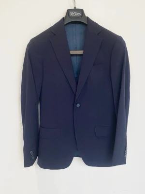 Oscar Jacobson Kostymsett - Marinblå Oscar Jacobson kostym, perfekt till suck/student! Nyskick, inga defekter. Storlek 44. Kavaj och byxor. Kontakta mig för fler frågor och funderingar!