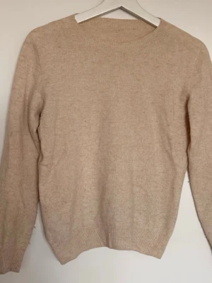 Ljusrosa stickad tröja i 100% Merinoull  - Mysig ljusrosa stickad tröja med rund hals och långa ärmar. Tröjan har ribbade muddar vid ärmslut och nederkant, vilket ger en klassisk och enkel look. Perfekt för lager på lager under kyliga dagar. 100% Merinoull. Lite nopprig som enkelt kan tas bort. 