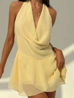 Ljusgul omlottklänning med öppen rygg - Söt ljusgul kortklänning i omlottmodell med draperad front och öppen rygg. Klänningen har tunna axelband och ett luftigt, svepande tyg som ger en somrig känsla. Perfekt för varma dagar och snygg att styla med smycken.