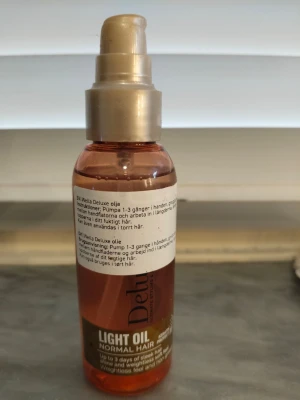 Wella Deluxe Light Oil för hår - Wella Deluxe Light Oil för normalt hår är en lätt hårolja i en genomskinlig plastflaska med pump. Oljan är gyllene och flaskan har detaljer i guld och brunt. Perfekt för att ge håret glans och mjukhet utan att tynga ner.
