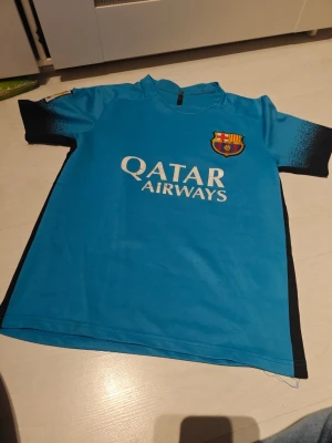 Blå FC Barcelona Messi tröja - Snygg blå fotbollströja från FC Barcelona med Messi och nummer 10 på ryggen. Framsidan har Qatar Airways-logga och klubbmärke, medan baksidan har UNICEF-tryck. Tröjan har svarta detaljer på ärmar och sidor, och är tillverkad i lätt och bekvämt material.