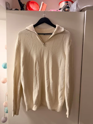 Beige stickad tröja med krage - Säljer en stilren beige stickad tröja med dragkedja vid halsen och bred krage. Tröjan har lång ärm och är ribbstickad vilket ger en snygg struktur. Perfekt för dig som gillar en enkel men trendig look.