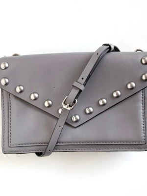 Grå axelväska med nitar från Rebecca Minkoff  - Snygg grå axelväska från Rebecca Minkoff i slätt läder med silverfärgade nitar på locket och justerbar axelrem. Väskan har en stilren, rektangulär form och detaljer i metall, inklusive en kedja på ena sidan. Perfekt för dig som gillar edgy och modern design.