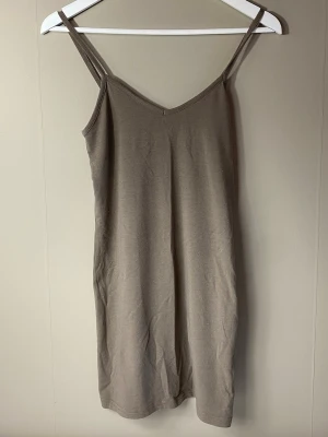 Beige ärmlöt långt linne/kort klänning - En enkel och stilren beige kortklänning/långt linne med smala axelband och v-ringad hals.