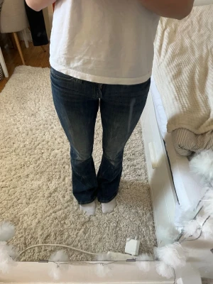 Mörkblå bootcut jeans - Säljer ett par mörkblå bootcut jeans med lätt slitning på framsidan och klassiska bakfickor. Jeansen har en snygg passform som sitter tajt över låren och släpper ut vid vaden. Perfekta till en avslappnad look och passar till det mesta.