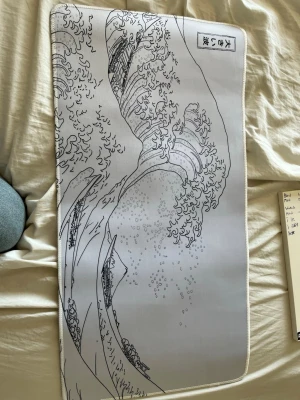 Stor musmatta med vågmotiv - Säljer en stor musmatta i tyg med motiv inspirerat av den klassiska japanska vågen. Färgen är ljusgrå med svart tryck och sydda kanter. Perfekt för gaming eller skrivbordet, ger bra glid för musen och skyddar bordet. Den är inte jätte stor så jag rekommenderar att inte ha tangentbordet på den för då får man lite utrymme för musen.