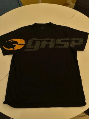 Svart GASP t-shirt med tryck - Cool svart t-shirt från GASP med stort tryck i grått och orange över bröstet. Klassisk rund hals och korta ärmar. Perfekt för dig som gillar sportig och avslappnad stil. Tillverkad i mjuk bomull för skön känsla hela dagen.