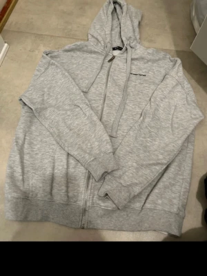 Ljusgrå zip hoodie från NewYorker  - Ljusgrå hoodie med dragkedja från Newyorker Klassisk modell med huva och dragsnören, samt fickor framtill. Diskret logga på bröstet och ribbade muddar vid ärmslut och nederkant. Den är i storlek M, den är oversized och jag har inte använt den särskilt mycket.