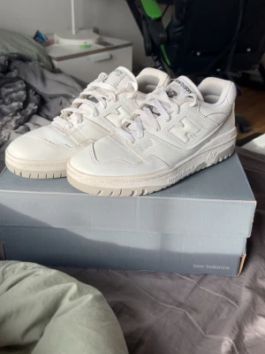 Vita New Balance 550 sneakers - Säljer ett par fräscha vita New Balance 550 sneakers i läder med klassisk siluett och tydliga NB-detaljer på sidan och tungan. Skorna har en chunky sula och vita skosnören, perfekta för dig som gillar stilrena och sportiga sneakers.
