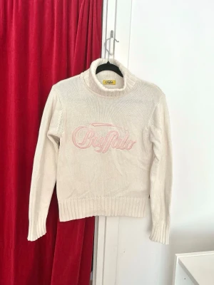 Buffalo vintage Y2K stickad polotröja - Buffalo vintage stickad polotröja i offwhite/creme med rosa broderad logga. Använt 1 gång, så nyskick! Så fin Y2K/00s vibe och sitter supersmickrande, lite croppad modell. Mjuk och skön, 100% bomull. Bra skick, inga hål eller fläckar. Storlek XS–S för tight fit. 