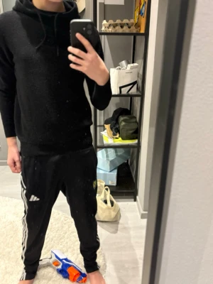 Svart hoodie med huva - En stilren svart hoodie med huva och dragsnören. Hoodien har en klassisk passform med långa ärmar och ribbade muddar vid ärmslut och nederkant. Perfekt för en avslappnad och enkel look. Materialet känns mjukt och bekvämt mot huden. Blanding mellan kashmir och ull. Ny pris 1000