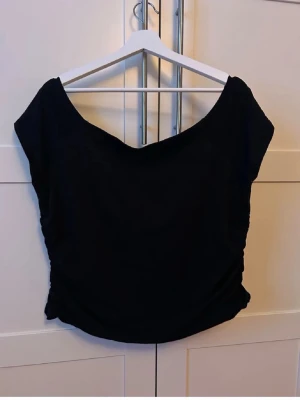 Offshoulder topp med rynkning - En svart, enkel och stilren offshoulder topp med rynkdetaljer på sidorna. Toppen är ärmlös och har en lätt loose passform. 