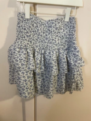 Blommig volangkjol från Zara - Enligt mig, är så pass stretchig så att det kan vara 164. Supersöt kjol från Zara med blått småblommigt mönster på vit botten. Kjolen har bred smock i midjan och dubbla volanger som ger en riktigt gullig och trendig look. Perfekt att matcha med en enkel topp för en fräsch outfit. Tillverkad i mjukt tyg.