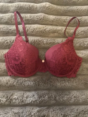Vinröd bh med spets och en liten rosett 75C - En snygg och skön bh i vinröd med spets på ifrån Lindex. Den har en liten ljusrosa rosett i mitten som lite extra💐Den har tvättats en gång men aldrig använt. Storlek 75C och nypriset är 340kr💕