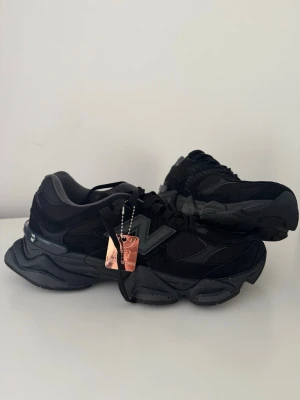Svarta New Balance 9060 sneakers - Stilrena svarta New Balance 9060 sneakers med chunky sula och mesh- samt mockadetaljer. Skorna har en stor grå N-logga på sidan och svarta skosnören. Perfekta för dig som gillar en sportig och modern look.