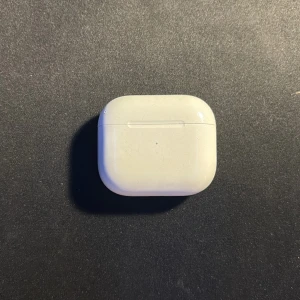 Apple AirPods med laddningsetui - Säljer ett par vita Apple AirPods gen 3 med trådlöst laddningsetui. Snygg och kompakt design i blank plast, perfekt för musik, poddar och samtal. Laddningsetuiet har en liten LED-indikator på framsidan. Smidig anslutning till iPhone och andra Apple-enheter.