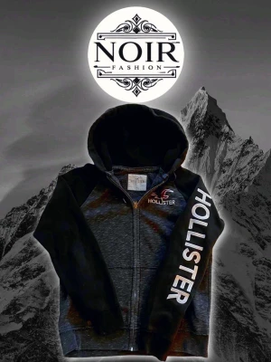 Svart hoodie från Hollister - Snygg svart zip-hoodie från Hollister med stor logga på ärmen och mindre logga på bröstet. Hoodien har dragkedja framtill, huva och ribbade muddar. Perfekt för en avslappnad och cool stil.