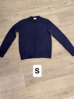 Mörkblå stickad tröja - En enkel och stilren mörkblå stickad tröja med rund halsringning och ribbade muddar vid ärmslut och nederkant. Perfekt att matcha med jeans eller kjol för en clean look.