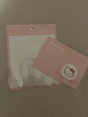 Hello Kitty brevpapper och kuvert - Säljer ett sött brevpapper och matchande kuvert från Hello Kitty. Setet är rosa och vitt med hjärtmönster och Hello Kitty-motiv. Perfekt för att skriva personliga brev eller hälsningar. Materialet är papper och designen är klassiskt kawaii.