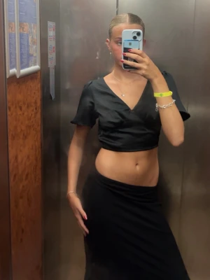 Svart omlottopp från Bik Bok - Snygg svart omlottopp från Bik Bok med croppad passform. Toppen har korta puffärmar, v-ringning och knytband både i ryggen och nedtill. Materialet är glansigt och känns lyxigt, perfekt för att lyfta din outfit.