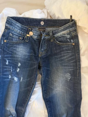 Low waist jeans från Eight Sin - Säljer ett par skit coola snygga low waist blå jeans från Eight Sin med slitningar och tvättade detaljer för en cool, avslappnad look. Klassisk femficksmodell med knappgylf och låg midja. Perfekta för dig som gillar streetstyle och vill ha ett par jeans med attityd.