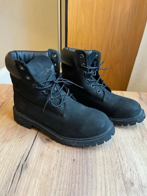 Svarta Timberland boots i mocka - Säljer ett par klassiska svarta Timberland boots i mocka med grov sula och snörning. Skorna har vadderad krage för extra komfort.  Storlek 39. Använt 1 gång då dom tyvärr va för små..  Har små synligheter på användning men i superfint skick, lite dammiga då dom stått ett tag☺️
