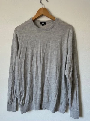 Ljusgrå Uniqlo tunn tröja från Uniqlo - Snygg ljusgrå långärmad tröja från Uniqlo i ett tunt och mjukt material. Tröjan har rund halsringning och ribbade muddar vid ärmslut och nederkant. Perfekt för lager på lager och enkel att matcha med olika stilar. 8D13