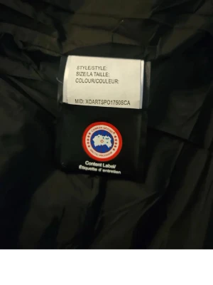 Svart Canada Goose dunjacka - Säljer en svart dunjacka från Canada Goose med klassisk patch på ärmen. Jackan har boxig passform, stora framfickor, hög krage och knäppning med både dragkedja och tryckknappar. Tillverkad i slitstarkt material och fylld med dun för maximal värme under vintern.