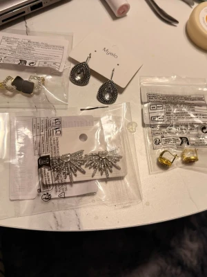 5 Mixade örhängen i olika stilar - Flera par örhängen i olika designer: ett par droppformade i silver med stenar från Myelo, ett par stjärnformade i silver, ett par med guldfärgade stenar, samt ett par med pärldetaljer och gråa inslag. Perfekt för dig som gillar att variera din stil.