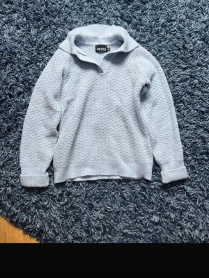 Ljusblå stickad tröja från Pieces - Ljusblå stickad tröja från Pieces med krage och v-ringning. Tröjan har lång ärm, uppvikta muddar och ett diskret strukturmönster i stickningen. Perfekt för lager-på-lager och enkel att matcha med jeans eller kjol.