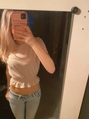 Ljusbeige croppad topp med volang - Säljer en ljusbeige croppad topp med korta ärmar och volangdetalj nedtill. Toppen har en elastisk midja som ger en snygg passform och är perfekt för dig som gillar en enkel och stilren look. Passar till jeans eller kjol.