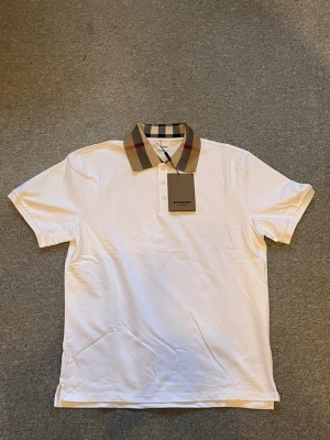 Vit Burberry piké  - Säljer en helt ny vit piké från Burberry med klassisk rutigt krage. Hör av er vid frågor