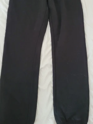 Svarta mjukisbyxor med resår - Ett par klassiska svarta mjukisbyxor med resår i bensluten. Byxorna har en rak passform och är tillverkade i mjukt och bekvämt material, perfekta för chill dagar. Inga synliga loggor eller detaljer. Passar dig som gillar enkel och avslappnad stil.