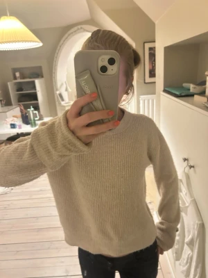 Beige stickad tröja med rund hals - Mysig beige stickad tröja med rund halsringning och långa ärmar. Tröjan har en enkel, rak passform och ribbstickade muddar vid ärmslut och nederkant. Perfekt för lager på lager och passar till det mesta i garderoben.