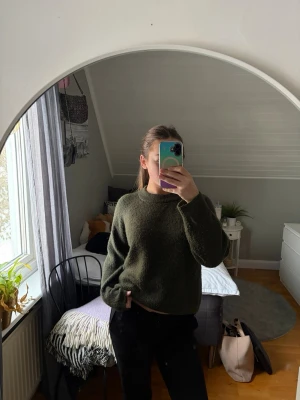 Mörkgrön stickad tröja - En enkel och snygg mörkgrön stickad tröja med rund hals och långa ärmar. Tröjan har en avslappnad passform och är perfekt att matcha med jeans eller kjol. Materialet ser ut att vara mjukt och lite fluffigt.