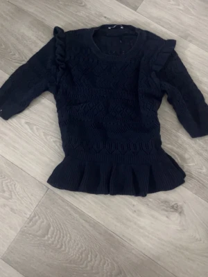 Mörkblå stickad topp med volang - Supersöt mörkblå stickad topp med volangkant nedtill och volangdetaljer på axlarna. Tröjan har ett fint mönsterstickat tyg och trekvartsärmar. Perfekt för dig som vill ha något gulligt och trendigt i garderoben🫰🏼💘