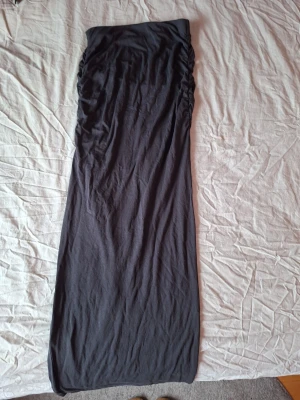 Svart långkjol med rynkade sidor - En svart långkjol med rynkade detaljer längs sidorna. Kjolen har en rak passform och är tillverkad i ett mjukt, stretchigt material som känns bekvämt mot huden. Perfekt för dig som gillar en enkel men snygg look.