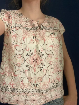 Mönstrad kortärmad blus💕🫰 - Söt blus i ljus bomull med rosa och svarta orientaliska mönster. Blusen har rund halsringning med liten knytning framtill och korta ärmar. Passar perfekt till jeans eller kjol för en avslappnad look.💞🪽