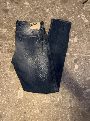 Mörkblå distressed jeans från Replay - Säljer ett par mörkblå jeans från Replay med coola slitningar, hål och unika blekta detaljer framtill. Jeansen har smal passform och klassisk femficksdesign. Perfekta för dig som gillar en edgy och trendig stil.