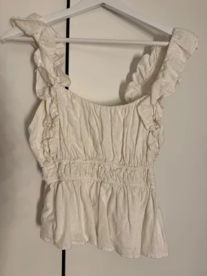 Vit volangtopp  - Söt vit topp med volangdetaljer på axelbanden. Sitter så fint och är perfekt nu till våren!🤩🥰😍😻